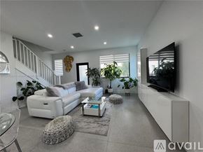 Doral townhouse for rent - A modern living room with a white sofa set, a glass coffee table, and a flat-screen TV mounted on the wall.
