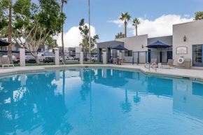 Phoenix apartment for rent - A large swimming pool in front of a building with a blue sky and palm trees in the background.