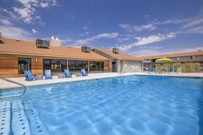 Mesa apartment for rent - A large outdoor swimming pool with lounge chairs and a building in the background.