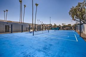 Phoenix apartment for rent - A tennis court with a blue surface and white lines, surrounded by palm trees and buildings.
