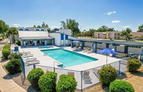 Phoenix apartment for rent - A swimming pool surrounded by a fence and bushes with a building in the background.