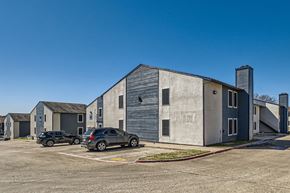 Dallas apartment for rent - A parking lot with cars and a large building in the background.