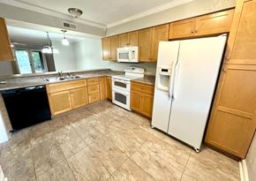 Simpsonville house for rent - A kitchen with a white refrigerator, black dishwasher, and wooden cabinets.