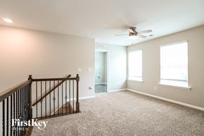 Troutman house for rent - A spacious room with a carpeted floor, a ceiling fan, and a staircase with a railing.
