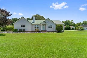 Sneads Ferry house for rent - A white house with a green roof and a chimney is surrounded by a green lawn.