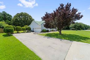 Sneads Ferry house for rent - A white house with a green roof is surrounded by a well-manicured lawn and trees.