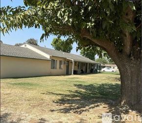 Merced apartment for rent - A tree is in the foreground of a house with a car parked in the driveway.