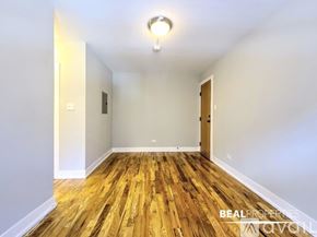 Chicago apartment for rent - A room with wooden flooring and white walls, with a light on the ceiling and a door on the right.