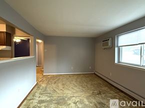 Petoskey apartment for rent - A room with a carpeted floor, a window with black curtains, and a wall-mounted air conditioner unit.