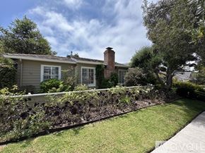 San Diego house for rent - A house with a grey exterior and a red brick chimney is surrounded by a well-kept lawn and a hedge.
