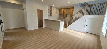 Ottawa apartment for rent - A spacious room with wooden flooring and a staircase on the right side.
