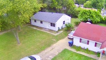 Louisville house for rent - A white house with a red roof is surrounded by green grass and trees.