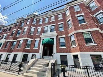 Boston apartment for rent - A red brick building with a green awning and a black fence in front.
