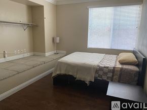Corona apartment for rent - A bedroom with a bed, a small table, and a window with blinds.