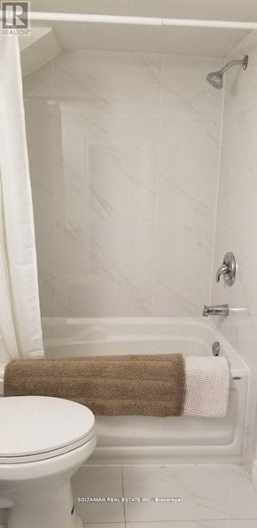 Toronto (West Hill) house for rent - A white toilet sits next to a white bathtub with a brown towel on the side.