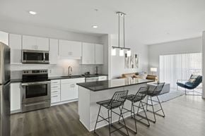 Fridley apartment for rent - Pet-Friendly Luxury Apartments In Fridley, MN - Axle Apartments - A Kitchen With White Cabinetry, Stainless Steel appliances, A Large Island With Bar Seating, And Sliding Glass Doors.