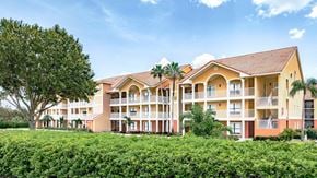Kissimmee apartment for rent - A large building with a red roof and balconies is surrounded by greenery.