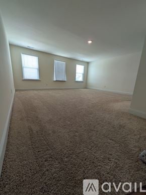 Angier house for rent - A carpeted room with two windows and a logo on the floor.