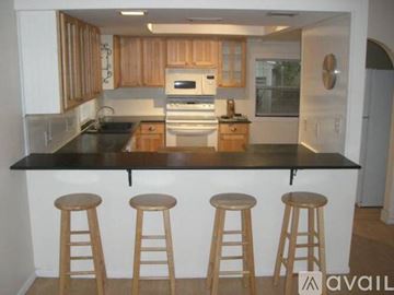 Sarasota house for rent - A kitchen with wooden cabinets and a black countertop with three stools.