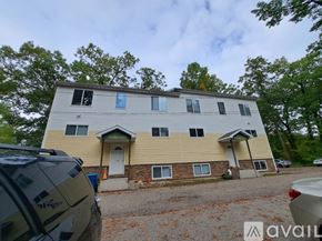 Kalamazoo house for rent - A two-story house with a beige and brown exterior is surrounded by trees and has a car parked in front.