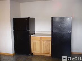Kalamazoo house for rent - Two black refrigerators in a room with a wooden cabinet.