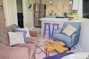 San Diego apartment for rent - A kitchen with a refrigerator, a sink, and a countertop with a blue chair and a couch with a pillow on it.
