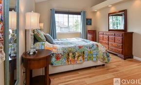 Arvada house for rent - A bedroom with a bed, a dresser, and a table with a lamp on it.