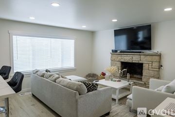 Seattle house for rent - A living room with a grey couch, a white coffee table, a fireplace, and a television mounted above it.