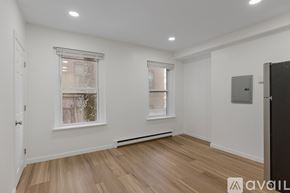 Boston apartment for rent - A room with wooden floors and white walls, a window with a view of trees, and a door on the right.