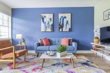 Davie apartment for rent - A living room with a blue couch, a wooden chair, a white coffee table, and two paintings on the wall.