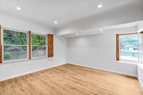 Northridge house for rent - A room with wooden floors and white walls, with windows showing a view of a fence and trees.