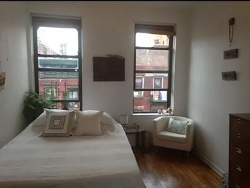 New York apartment for rent - A bedroom with a bed, chair, and two windows.