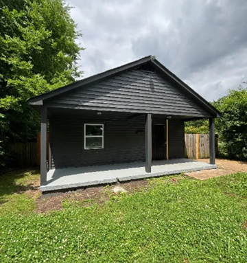 Memphis house for rent - A small house with a grey roof and a white door is surrounded by greenery.