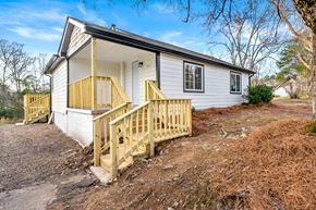 Lithonia house for rent - A small house with a wooden deck is surrounded by trees and grass.