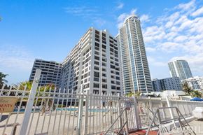 Hollywood apartment for rent - A white fence surrounds a pool in front of a large building.