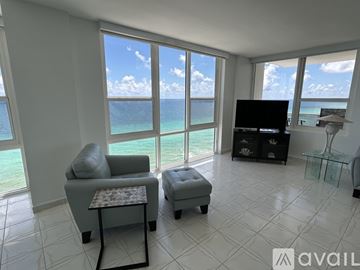 Hollywood apartment for rent - A living room with a grey sofa and ottoman, a flat screen TV, and a view of the ocean through the windows.