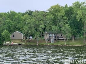 Long Prairie house for rent - A house is situated on a lake surrounded by trees.