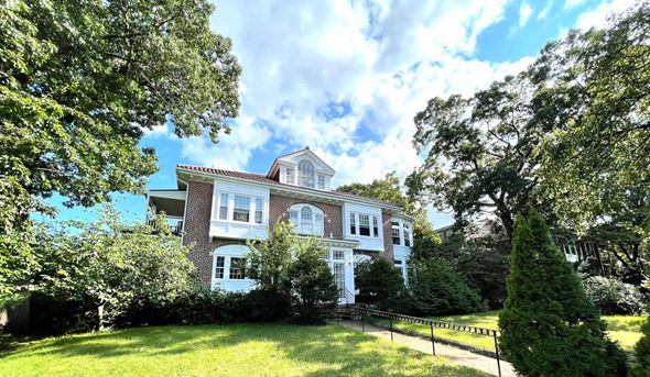 Boston apartment for rent - A large white house with a red brick chimney is surrounded by green trees.