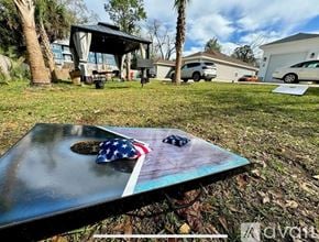 Pensacola house for rent - A flag-themed table with a small American flag and a black object on it is in the foreground of a yard with a house and vehicles in the background.