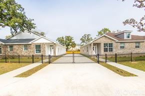 Pensacola house for rent - A row of houses with black fences and green trees in front.
