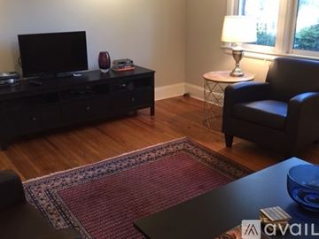 Charlotte townhouse for rent - A living room with a black leather chair, a black entertainment center, a red and white rug, and a small white table with a lamp on it.