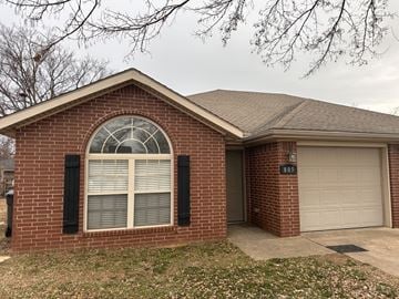 Rogers house for rent - A brick house with a white garage door and a window with black shutters.