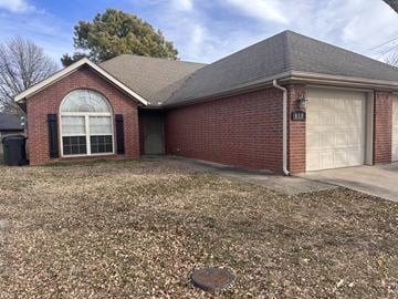 Rogers house for rent - A red brick house with a white garage door and a window with black shutters.