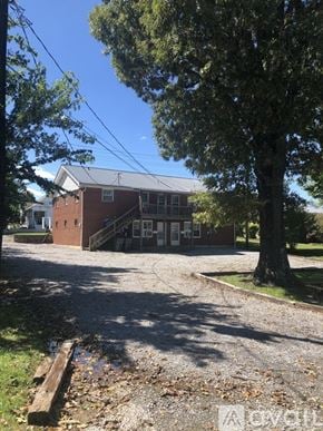 Dickson apartment for rent - A building with a red brick exterior and a grey roof is surrounded by trees and a gravel driveway.