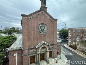 Cambridge apartment for rent - A large brick building with a clock tower is surrounded by trees and other buildings.