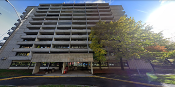 Ottawa apartment for rent - A tall concrete building with a tree in front of it.