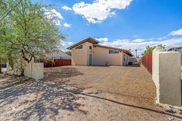 Tucson house for rent - A house with a brown roof and a blue sign on it is surrounded by a dirt area and a tree.