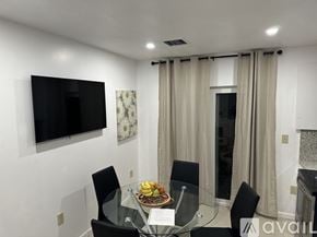 Miramar apartment for rent - A modern dining room with a glass table and chairs, a flat screen TV, and a window with curtains.