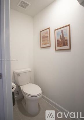 Miami townhouse for rent - A white toilet in a small bathroom with two pictures on the wall.