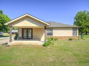 Harrah house for rent - A house with a brown roof and a stone wall in front.